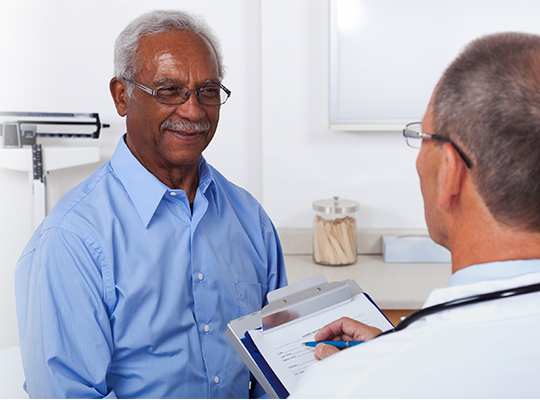 在医生的办公室里，一位成熟的男医生一边和一位微笑的老年病人交谈，一边在剪贴板上写着什么。