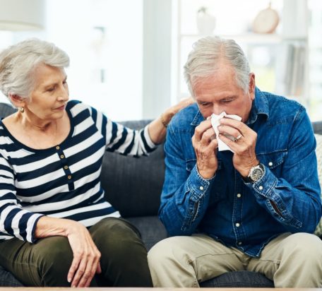 一位老人正在擤鼻涕，他的妻子在沙发上安慰他。