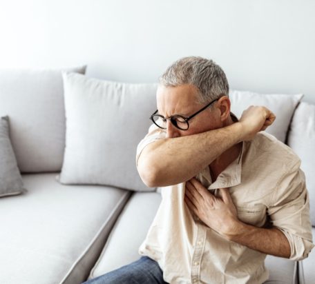 一个坐在沙发上的成年男性咳嗽到肘部。