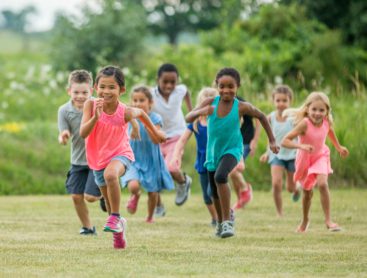 A group of young children running outside smiling while playing tag.